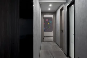 A modern corridor with concrete flooring and metallic walls, featuring a dark door and glass doors on the right side.