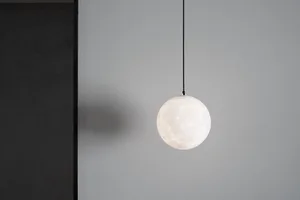 A minimalist glass sphere pendant light hanging from a black cord against a gray wall.