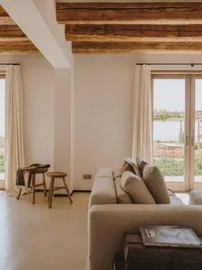 A minimalist living room featuring wooden beams, concrete floors, and upholstered furniture with fabric cushions.