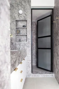 Modern bathroom interior with marble walls and black-framed glass shower enclosure.
