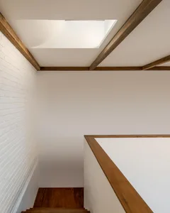 A modern interior space featuring wooden stairs, white brick walls, and white-painted columns.