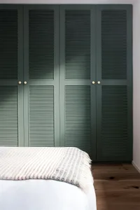 Minimalist bedroom with wooden flooring and a partially visible bed with a white and beige striped blanket.