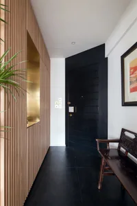 A modern entryway featuring black wooden walls and flooring, with a black door and wooden bench.