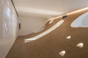 A modern interior space with curved surfaces and lighting, featuring a projection screen with visual content on the left wall