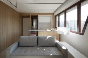 A minimalist residential interior with light-colored wood, white accents, and stainless steel kitchen appliances.