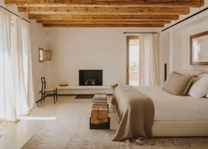 A minimalist bedroom featuring a bed with sandy-colored sheets, wooden furnishings, and sandstone elements.