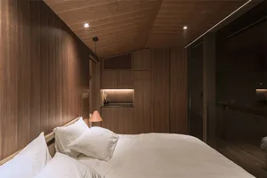 A minimalist bedroom with a bed, white bedding, and wood walls and ceiling.
