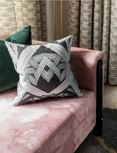 A modern couch with a pink velvet upholstery and patterned pillows against a backdrop of striped curtains and a patterned flo