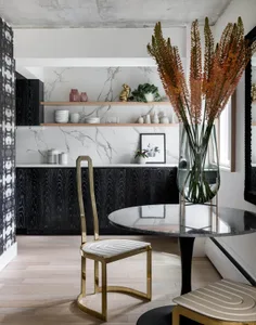 Contemporary dining area with marble countertops, glass vase with orange flowers, and black and gold metallic chairs.