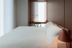 A modern minimalist bedroom with a large bed, wooden headboard, and red pendant lights.