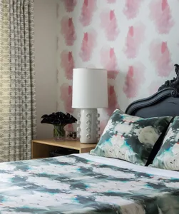 Modern bedroom with a patterned bedspread, floral pillows, and a white lamp on a wooden shelf.