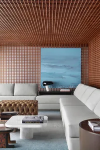 A modern living room with a white sectional sofa, a brown tufted ottoman, wooden lattice walls, and a large blue abstract pai