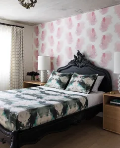 A modern bedroom featuring a bed with patterned bedding and a headboard, against a wall with pink and white patterned wallpap
