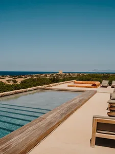 A modern residential exterior featuring a wooden-edged swimming pool overlooking the sea.