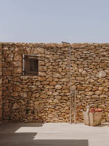 An outdoor shower with a stone wall and wooden floor.