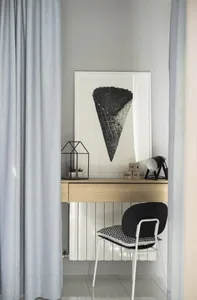 A minimalist office space featuring a wooden desk, black and white chair, and an art piece of an ice cream cone hanging above