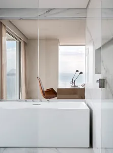 A minimalist bathroom featuring a white marble bathtub with an ocean view.
