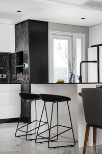 Modern kitchen with black and white marble countertops and black stools.