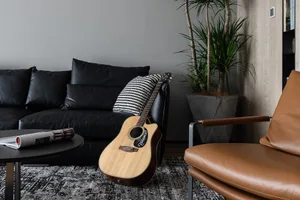 A modern living room with black leather sofa, acoustic guitar, and potted plant.