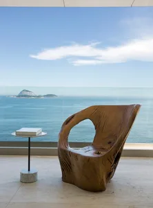 Modern, sleek lounge chair crafted from textured, dark wood on a sleek, minimalistic patio overlooking the ocean.