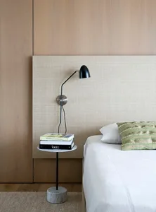 A minimalist bedroom with textured walls, a white bed, and a small side table with books and a lamp.