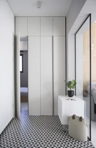A minimalist bedroom with a black and white geometric floor, white furniture, and a glass partition.