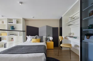 A minimalist bedroom with a white bed, yellow accents, and a wooden floor.