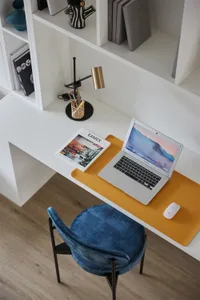 Minimalist home office setup with a white desk, yellow mouse pad, and blue chair.