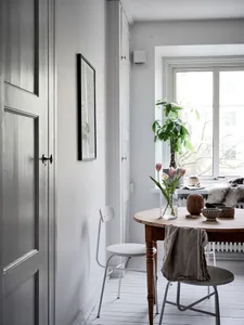 Modern, white minimalist interior with wood dining table and chairs, minimalist art, and a plant on the window sill.