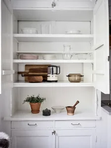 Minimalist kitchen storage featuring wooden chopping boards, glass pitchers, ceramic bowls, and white cabinets.
