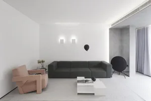 A minimalist living room featuring a gray sofa, a white coffee table, and a pink armchair.