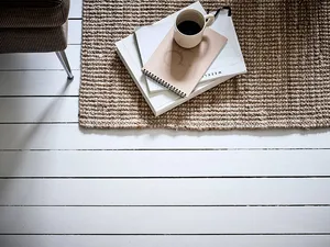 A minimalist workspace featuring ceramic floor tiles with a stack of notebooks and a cup of coffee on a textured wool rug.