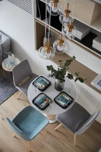 Modern dining room with metal and glass table, wooden chairs, and potted plant.