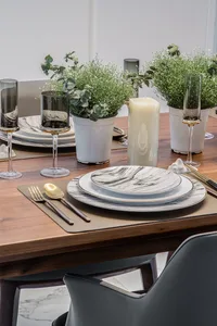 A modern dining table set with marble plates, wooden chairs, and greenery decor.