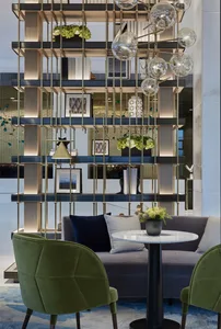 Modern lobby with a geometric design featuring sleek furniture, green chairs, and a round table with a vase of flowers.