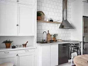 A modern minimalist kitchen with white cabinets, tiled backsplash, and stainless steel appliances.