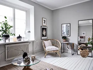 A modern minimalist living room with white walls, a wicker chair, a glass coffee table, and a large window.