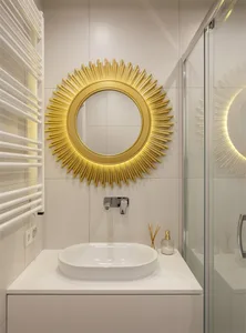 Modern minimalist bathroom with white ceramic tiles, sunburst mirror with gold accents, and a sleek white sink.