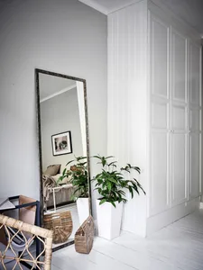 A modern minimalist living room with white flooring, wood furniture, and a tall floor mirror.
