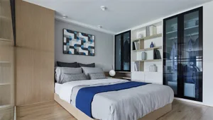 Modern bedroom with white walls and bed, featuring a blue and white geometric artwork on the wall.