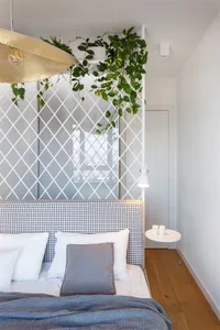 A modern bedroom with a plaid upholstered bed, blue blankets, and green plants hanging from the ceiling.