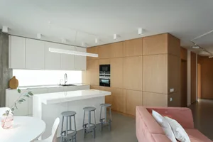 Modern minimalist kitchen with white laminate countertops, wood cabinets, and a bar counter with stools.