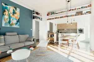 A minimalist living room featuring a gray sofa, white chairs, a modern wooden table, and white bookshelves filled with books.
