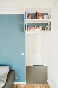 A modern living room featuring hardwood floors, floating shelves, and a blue accent wall.