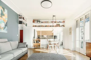 A modern living room with wooden floor, white walls, and white shelves filled with books and decor items.