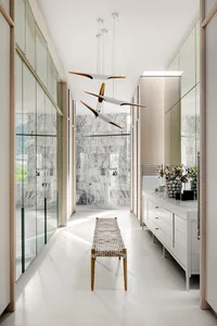 Modern bathroom with white marble walls, white floor, white bench, and white cabinetry with metallic accents.