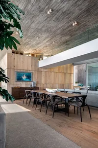 An industrial-style dining room featuring a long wooden table surrounded by black chairs, with a wooden ceiling and walls, an