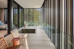 A modern minimalist balcony with wooden flooring and metal railings overlooking a green landscape.