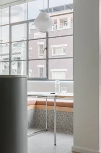 Modern cafe interior featuring a white cushioned seating area with a white table and vase, set against a backdrop of a glass 