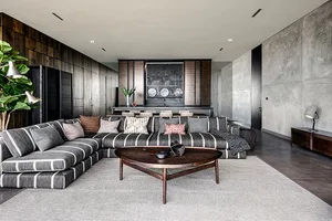 Modern living room with grey sectional sofa, wooden coffee table, and concrete textured walls